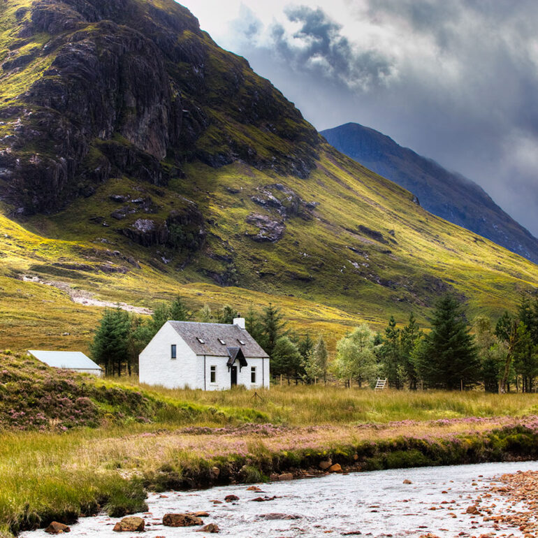 A small cottage along a stream at the foot of a mountain.