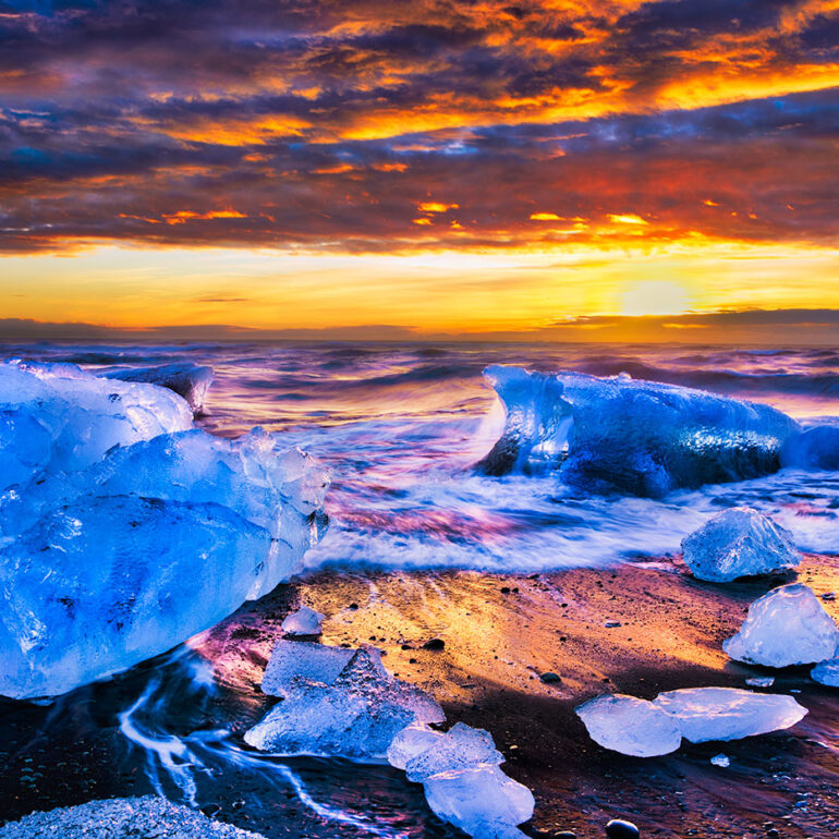 Blue chunks of ice washed up on a black beach at sunrise.