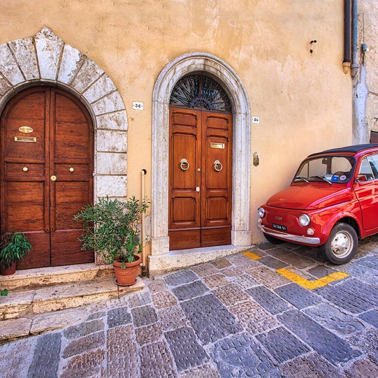 Small red car in fron of doorway in Tuscany.