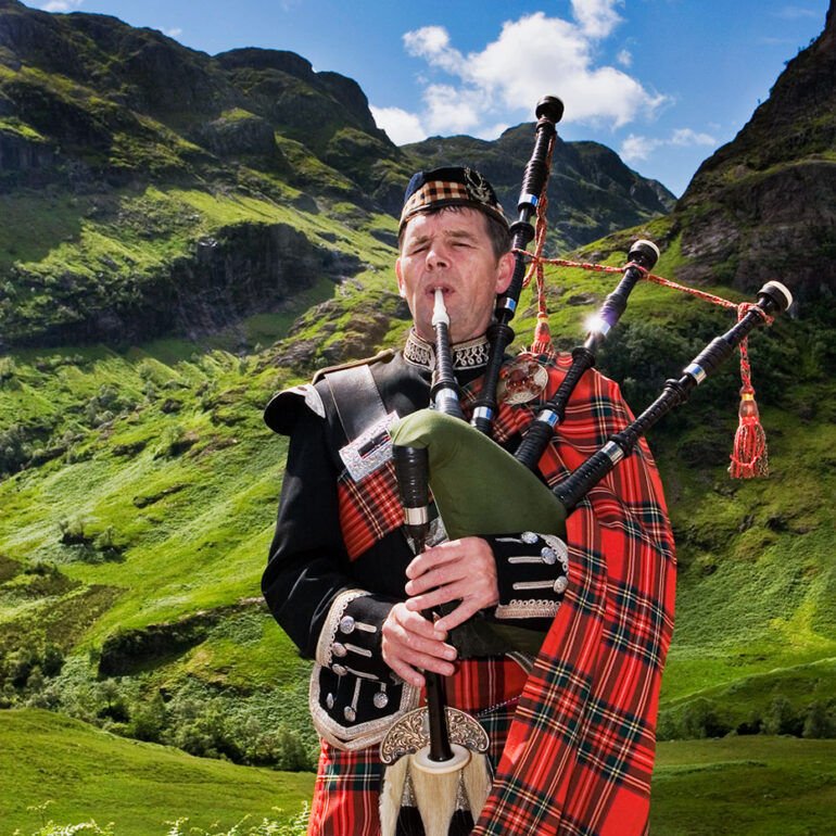 A bag piper playing in front of a mountain.