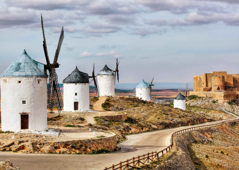 Windmills on a hill with a castle in the background.