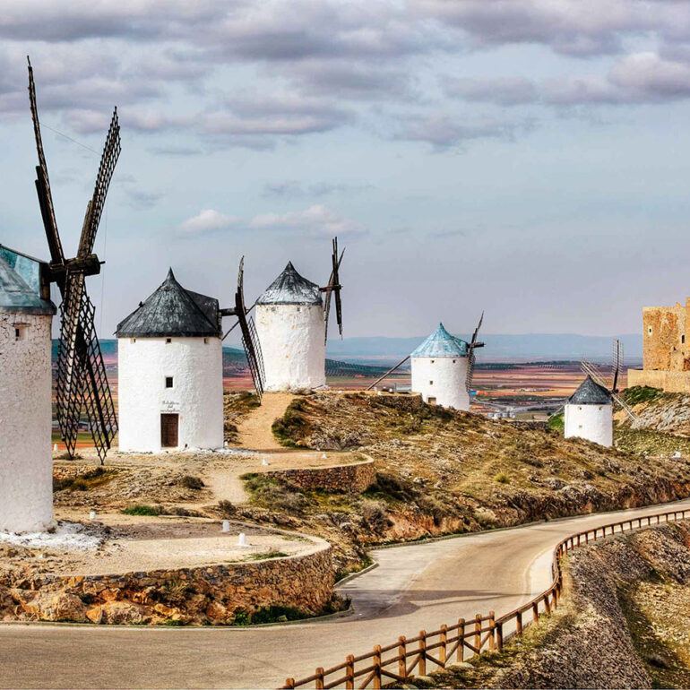 Windmills on a hill with a castle in the background.