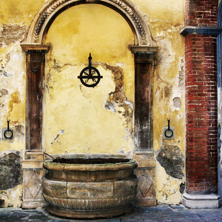 Old well set into a wall with cracking yellow paint.